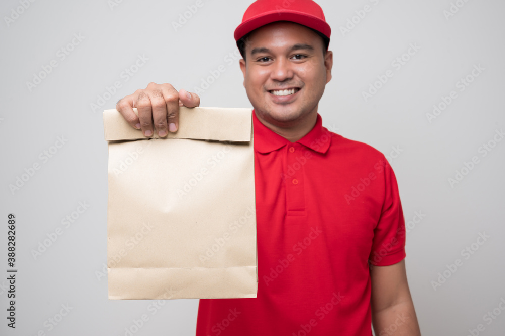 Young smiling asian delivery man in red uniform holding paper bag food delivery on isolated white background.