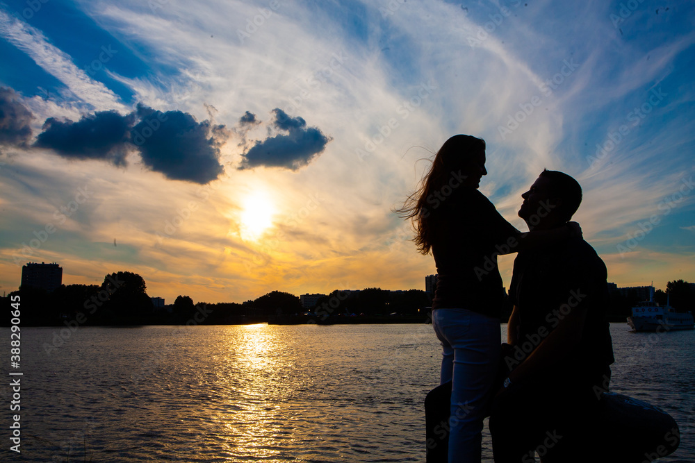  Silhouette of a loving couple cuddling during a golden sunset reflected in the water, showing the concepts of love, couple, romance, valentine, togetherness