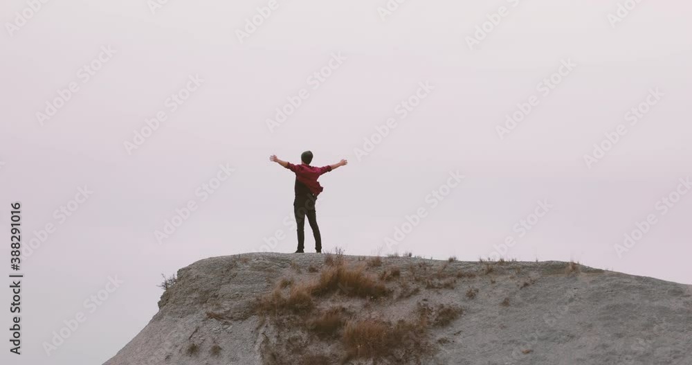 Male hiker, wearing skull cap and red shirt, raising arms up on top of a rocky mountain. Enjoying nature and looking in the sky. Freedom, Feeling blessed, happy. Achievement goal succeed concept. Male hiker, wearing skull cap and red shirt, raising arms up on top of a rocky mountain. Enjoying nature and looking in the sky. Freedom, Feeling blessed, happy. Achievement goal succeed concept.