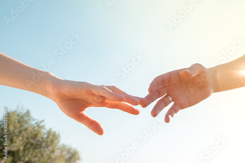 two hands with wedding rings against a blue clear sky are reaching out to each other.. © SValeriia