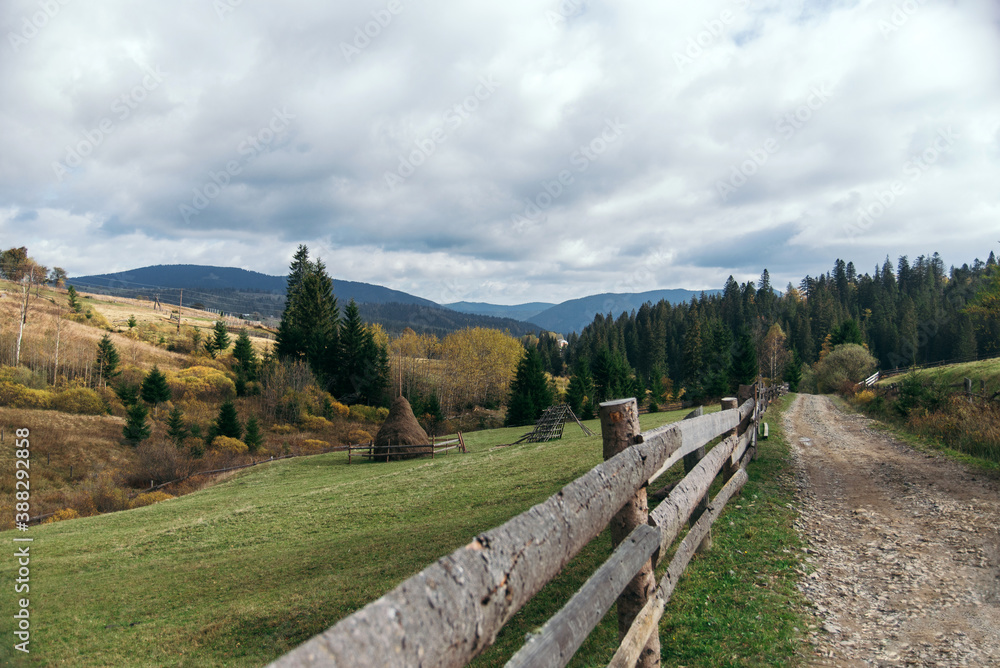 Beautiful autumn landscape of the Carpathian village in the mountains and a path along the fence. haystacks and coniferous forest