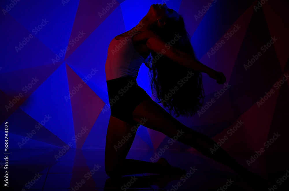Woman dancing on the background of a beautiful multicolored wall. Sexy slim lonely girl with long black hair. female holds her head. bright colorful geometry background.