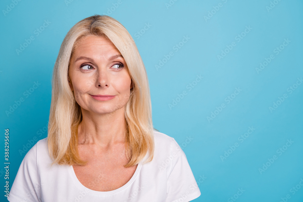 Photo of attractive aged lady good mood look side empty space wear casual white t-shirt isolated blue color background Photo of attractive aged lady good mood look side empty space wear casual white t-shirt isolated blue color background