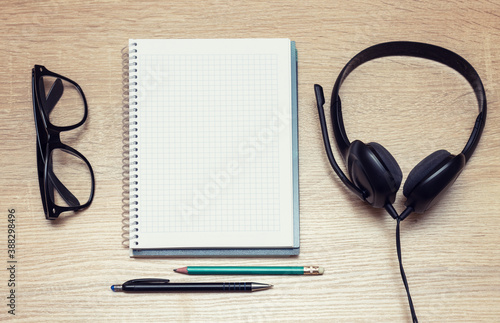 Online training. Top view student's desk with headphones, glasses, notepad, pen and pencil. Listening and taking notes of audio books.