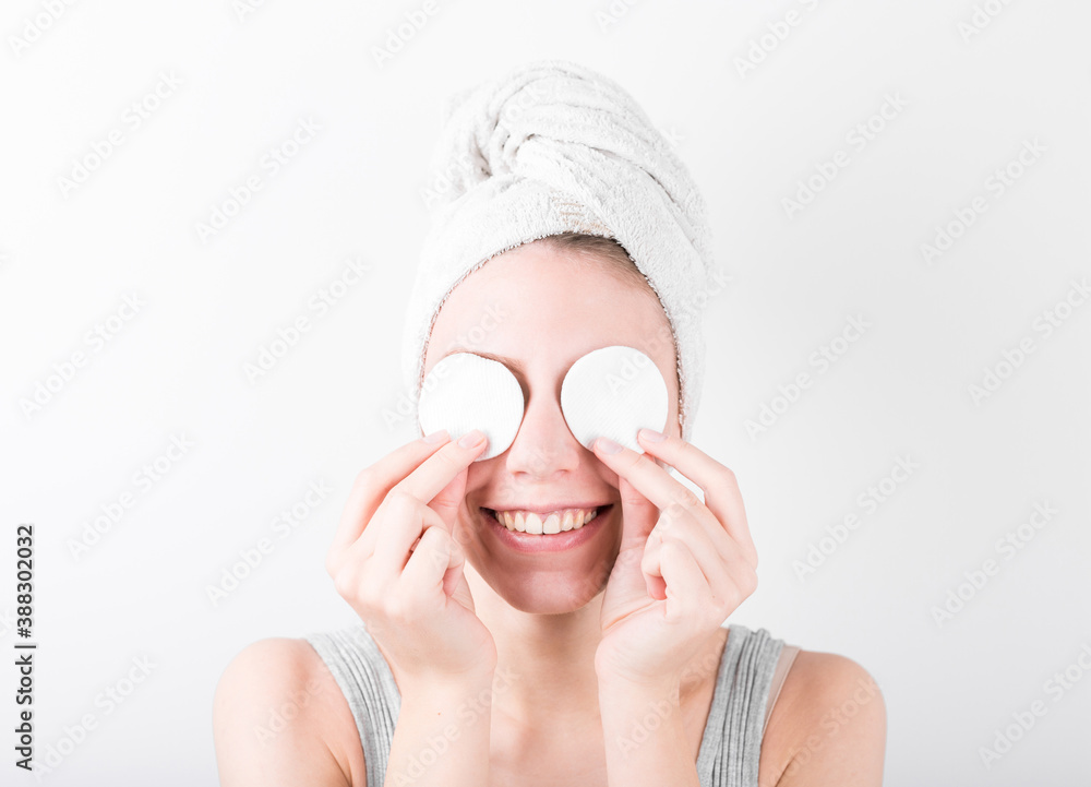 Close up beauty portrait of a smiling attractive woman cleaning her face with a cotton pad isolated over white background Close up beauty portrait of a smiling attractive woman cleaning her face with a cotton pad isolated over white background