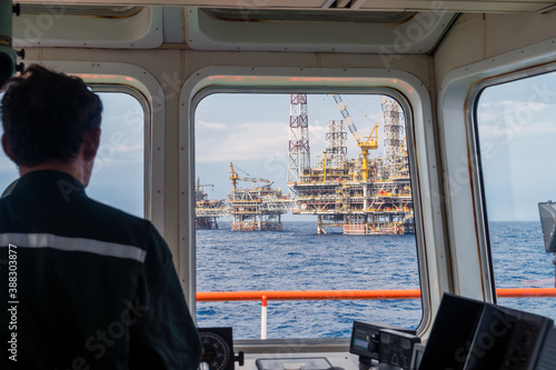 A supply boat captain maneuvering his vessel from forward bridge while heading to a production platform for transferring material and equipment at Terengganu oil field.