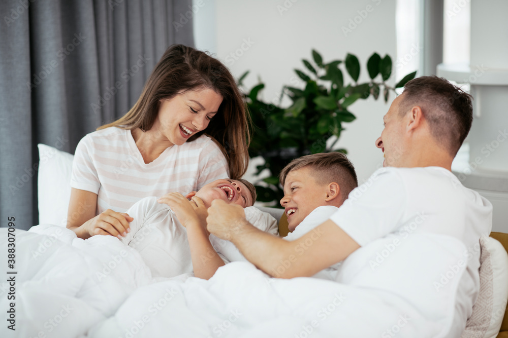 Young family enjoying in bed. Happy parents with sons relaxing in bed.