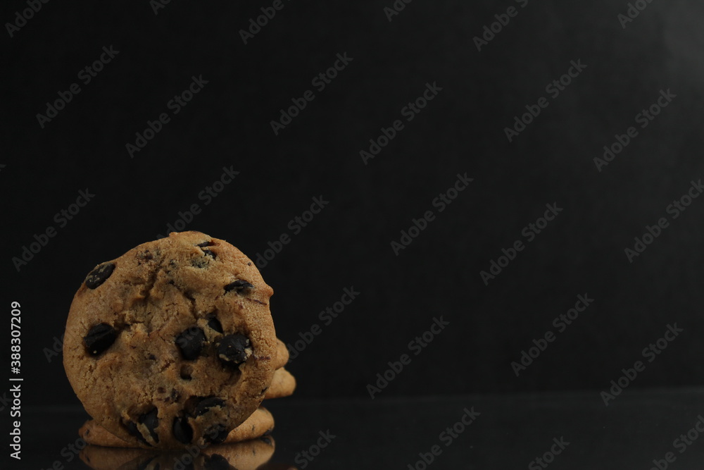 food background cookies round with chocolate drops lying standing on the edge of the edge with a reflection on a black dark mirror background side view of copy space food background cookies round with chocolate drops lying standing on the edge of the edge with a reflection on a black dark mirror background side view of copy space