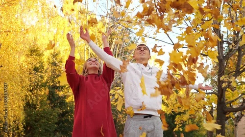 Positive young couple throw armfuls of dry bright yellow leaves and hugs in autumn park slow motion photo