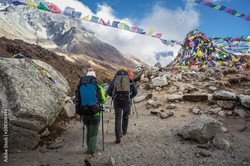 Backs of two trekkers who pass by the memorial in with religious flags in honor of alpinists died on the Everest mountain. Sad place.