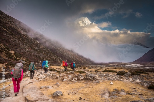 Group of trekkers walk along Khumbu valley. Ama Dablam mountain (6812m) covered with snow and light clouds is on the background. Nepalese Himalayas.