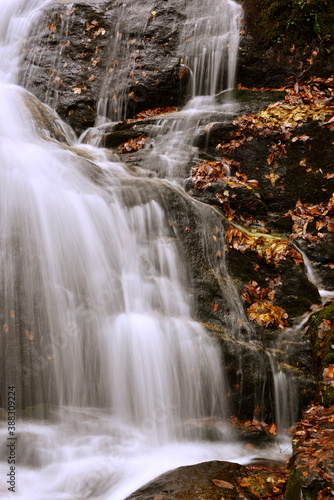 Cascading water splashing over granite rocks with colorful autumn leaves creates a tranquil scene.