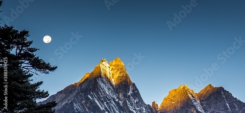 Amazing early morning: golden sun lights high peak of Kongde Ri mountain of the Himalaya, one of the most difficult mountains to climb. Moon shines above the summit. Himalayas, Nepal. photo