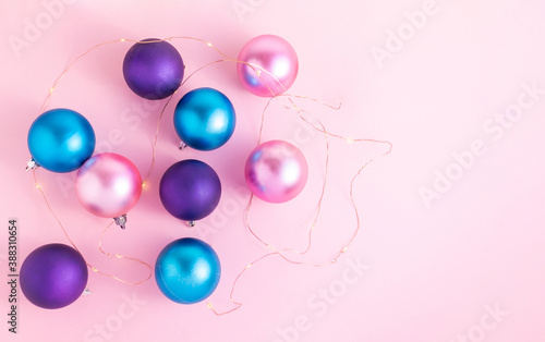 Fototapeta Naklejka Na Ścianę i Meble -  Pink, turquoise and purple satin Christmas balls on a pink background with small lights around them. Christmas decoration for ideal for the New Year's Eve and New Year