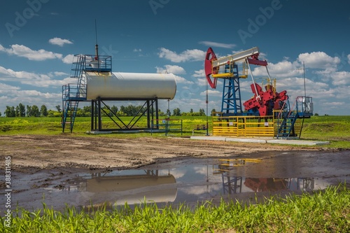 ULYANOVSK, RUSSIA - JUNE 30, 2017: Oil pump  at oil field in Ulyanovsk region and oil puddle at the foreground. Summer. Bright blue sky with white clouds. photo