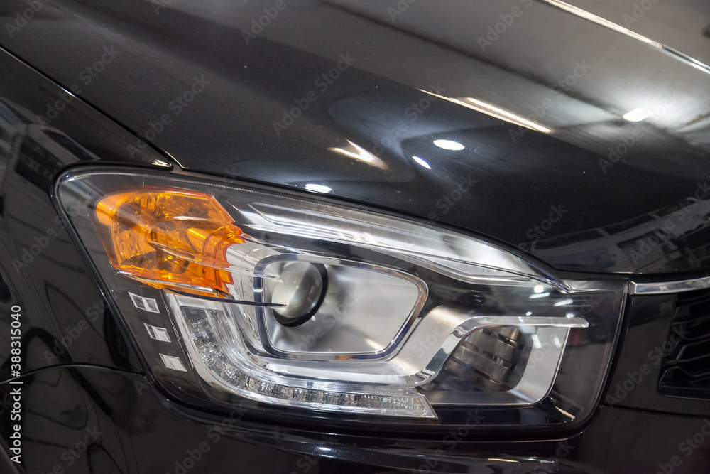 A view of a dark blue car headlight after cleaning and polishing before being sold. Large vehicle lamp with xenon lens. Auto-parsing car in the garage. A view of a dark blue car headlight after cleaning and polishing before being sold. Large vehicle lamp with xenon lens. Auto-parsing car in the garage.