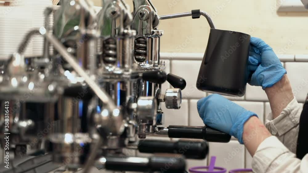 Barista is making coffee in coffee machine using protective gloves and a mask. Barista is making coffee in coffee machine using protective gloves and a mask.