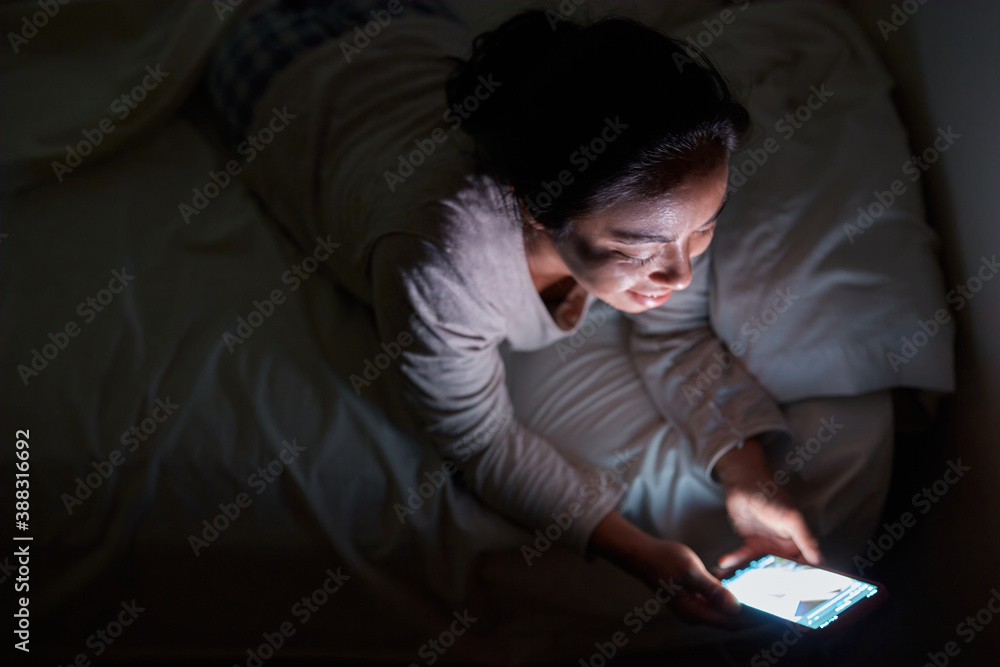 Mujer joven acostada en su cama texteando y navegando por la web en la noche Mujer joven acostada en su cama texteando y navegando por la web en la noche