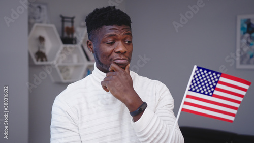 Young thoughtful black man holding usa flag. Asylum seeker thinking about job opportunities in USA. High quality photo