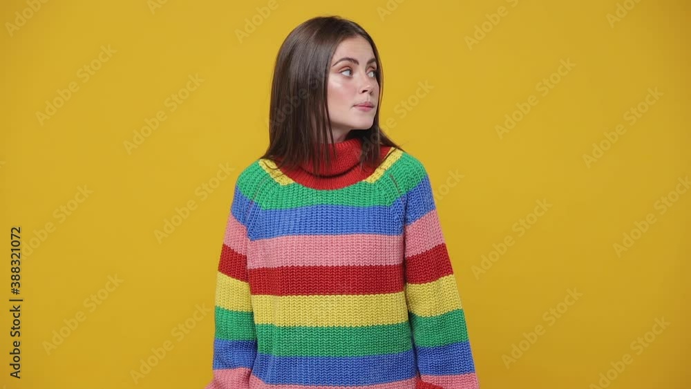Secret young woman 20s years old in colorful sweater posing isolated on yellow background studio. People lifestyle concept. Looking aside saying hush be quiet with finger on lips shhh gesture blinking