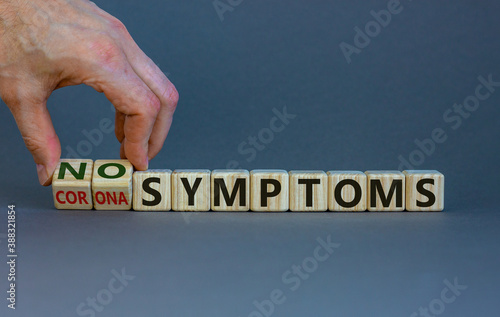 Hand turns cubes and changes the words 'corona symptoms' to 'no symptoms'. Beautiful grey background. Copy space, medical and covid-19 pandemic concept.