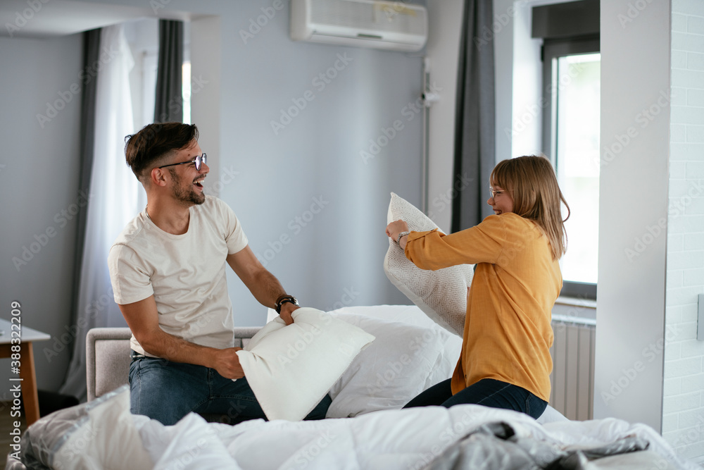 Fototapeta premium Husband and wife fighting pillows on the bed. Young couple having fun at home.