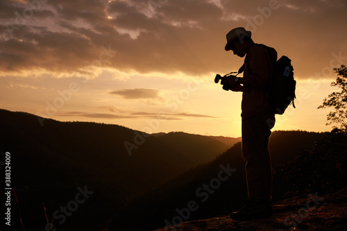 Silhouette teenager checking a photograph in camera on the edge of a cliff