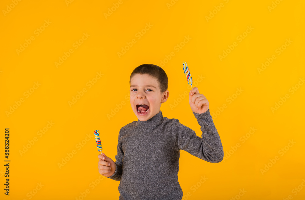 happy little boy with two lollipops on a yellow background with space for text happy little boy with two lollipops on a yellow background with space for text