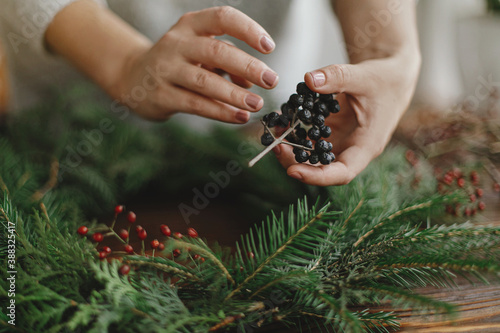 Florist hands holding berries and making rustic christmas wreath on wooden table