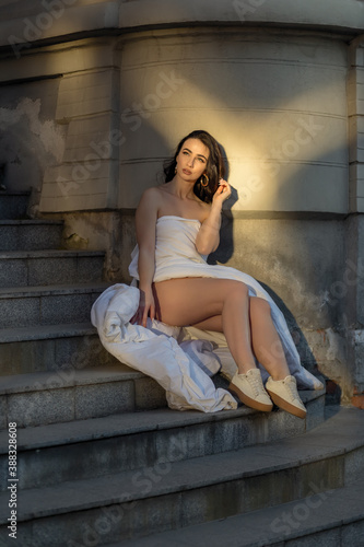 people, rest, comfort and leisure concept - Young woman through the evening streets wrapped in a blanket. Portrait of young woman sits on the steps of an old building at dawn