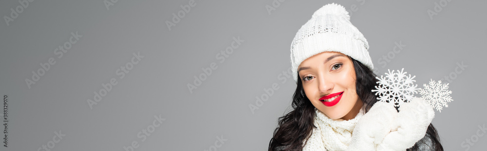 joyful and brunette woman in winter outfit looking at camera and holding snowflakes isolated on grey, banner joyful and brunette woman in winter outfit looking at camera and holding snowflakes isolated on grey, banner