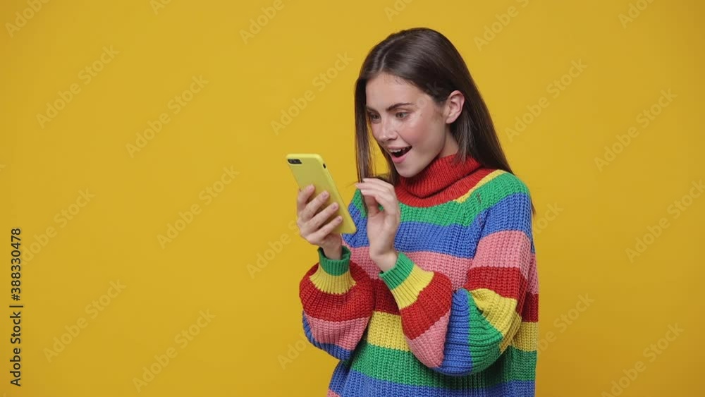 Shocked amazed young woman 20s years old in colorful sweater isolated on yellow background studio. People lifestyle concept. Using mobile cell phone typing sms mesage browsing say wow put hand on head Shocked amazed young woman 20s years old in colorful sweater isolated on yellow background studio. People lifestyle concept. Using mobile cell phone typing sms mesage browsing say wow put hand on head