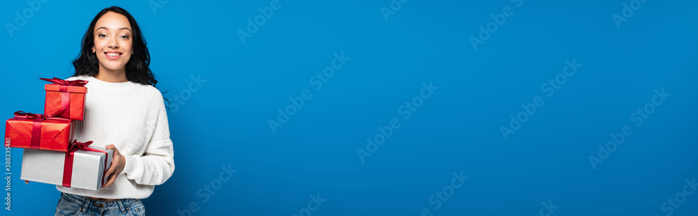 happy woman in knitted sweater holding gift boxes isolated on blue, banner happy woman in knitted sweater holding gift boxes isolated on blue, banner