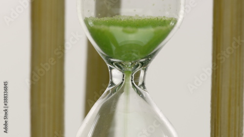 Close up hourglass countdown isolated on white background. Light green sand falling move through sandglass. Passing time, deadline, loading, timer, earth care save life concept, time is over. Zoom in