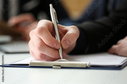 Hand of businessman in suit filling and signing with silver pen partnership agreement form clipped to pad closeup. Management training course, some important document, team leader ambition concept