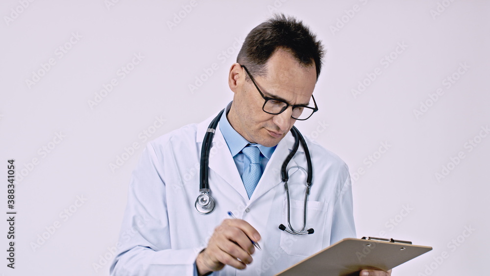 Handsome serious doctor in uniform takes pen from his pocket writes prescription on clipboard isolated white background. Healthcare, medicine, health, medical specialist, patient diagnosis concept Handsome serious doctor in uniform takes pen from his pocket writes prescription on clipboard isolated white background. Healthcare, medicine, health, medical specialist, patient diagnosis concept