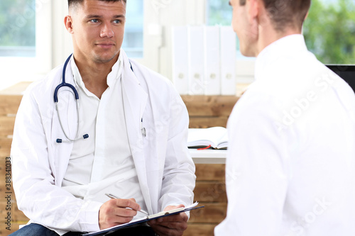 Handsome male medicine doctor with clipboard pad in hands examine patient and prescribe remedy. Exam, visitor reception, disease prevention, ward round, visit check, 911, healthy lifestyle concept