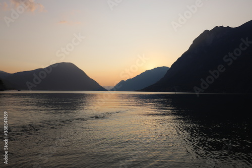 Colorful sunset in Italy over a mountain range with still lake in foreground during golden hour in late summer.