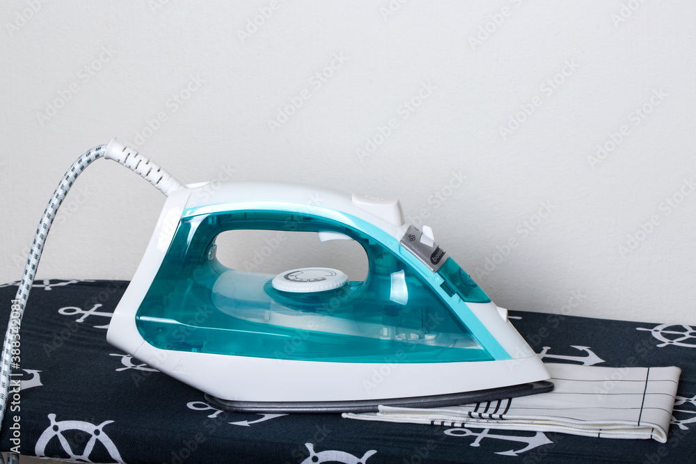 Folded ironed colorful cotton clothes lie next to the iron on white