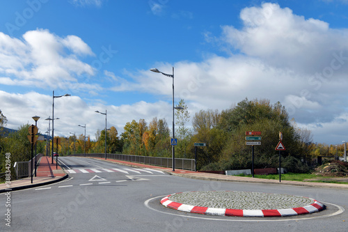 View of traffic circle or roundabout and empty paved road lined with street lamps and trees.