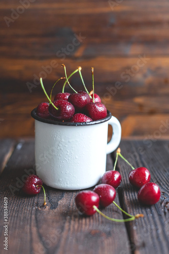 Fresh red ripe organic macro sweet cherry with waterd drops in a white cup on wooden background. space for text. closeup photo