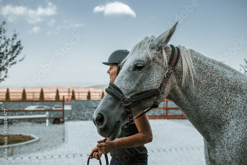 Cropped photo of young brunette felmale competitor with Arabian thoroughbred horse. Hors riding equipment
