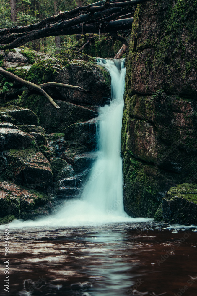 Naklejka premium Picturesque waterfall in the middle of the Czech wilderness. An inaccessible place hides this colorful wealth. Waterfall on the river Jedlova, photographed for a long exposure time.