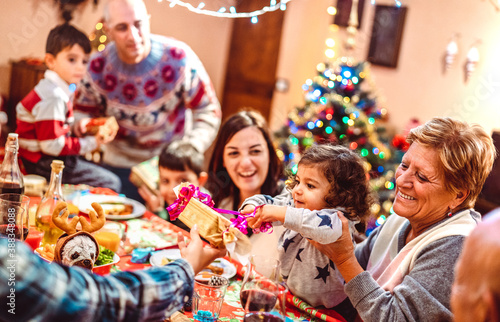 Multi generation big family having fun at christmas supper party - Winter holiday x mas concept with parents and children eating together opening gifts at home - Focus on little daugther - Warm filter photo