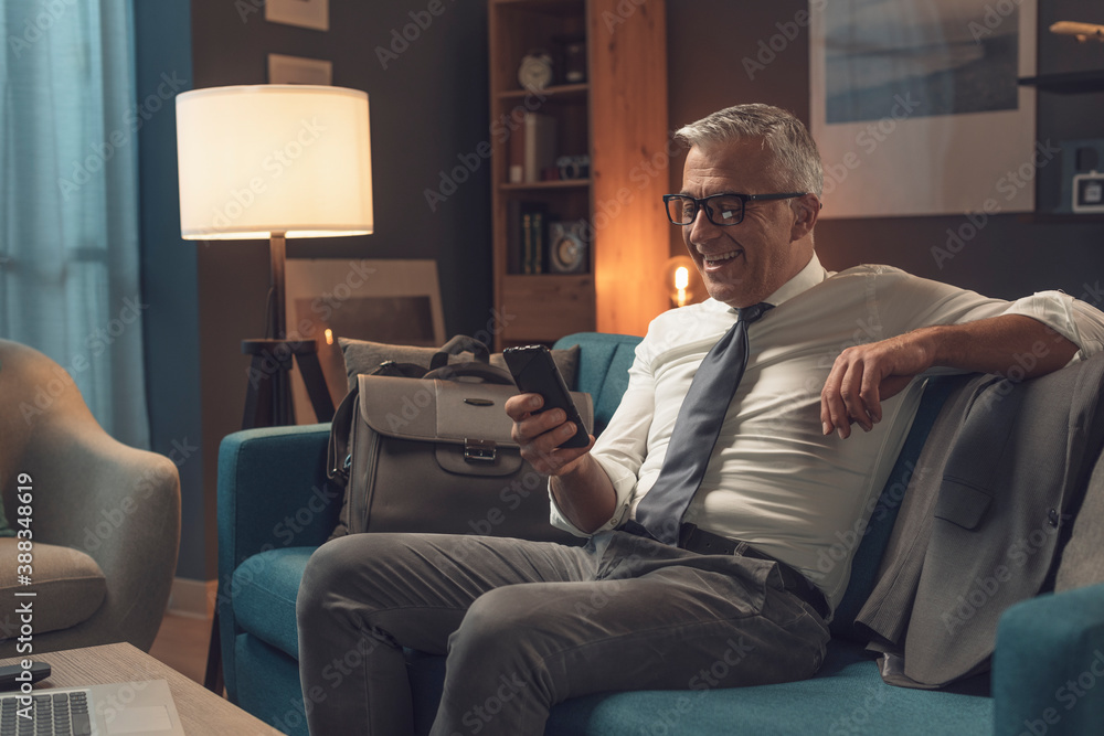 Fototapeta premium Businessman relaxing on the sofa at home and connecting with his phone