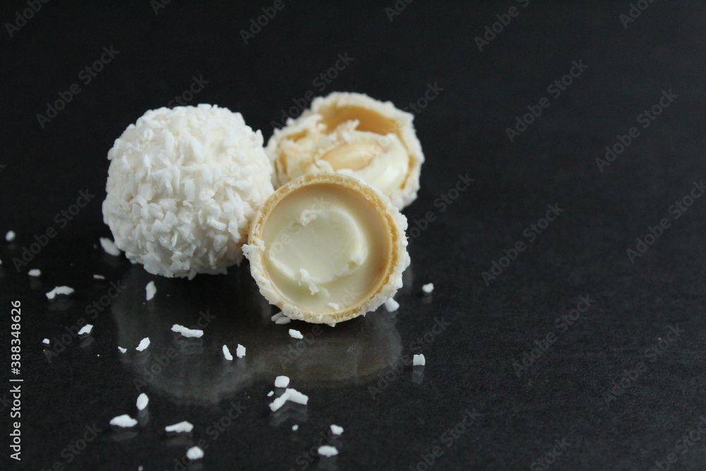 one two three a few white candies in a coconut sprinkle like Raffaello on a glossy black background with a reflection there is a copy space for the text one two three a few white candies in a coconut sprinkle like Raffaello on a glossy black background with a reflection there is a copy space for the text
