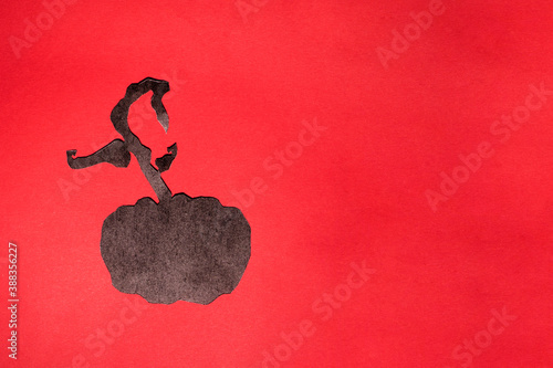 Black colored cut out craft pumpkin on a red background. Photo of paper art with text for your scary Halloween design. There is a place for text, photo