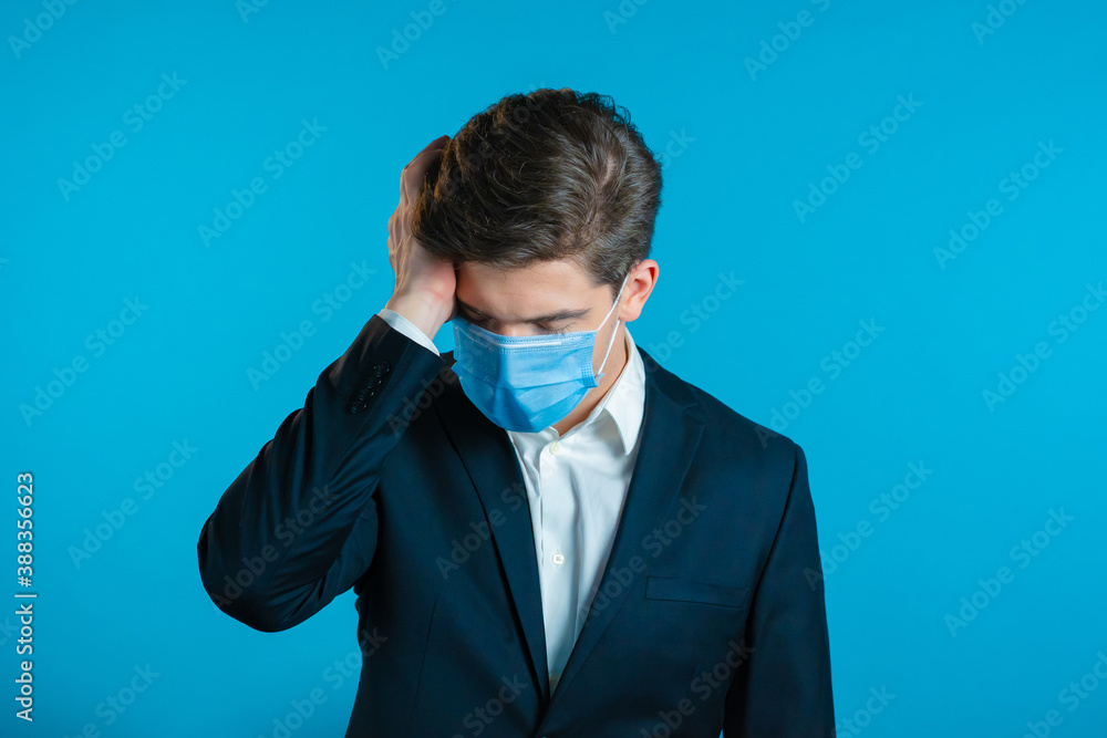 Frustrated european business man in suit and protective mask over blue wall background. Guy is tired, bored of work or studying, he disappointed, helpless Frustrated european business man in suit and protective mask over blue wall background. Guy is tired, bored of work or studying, he disappointed, helpless
