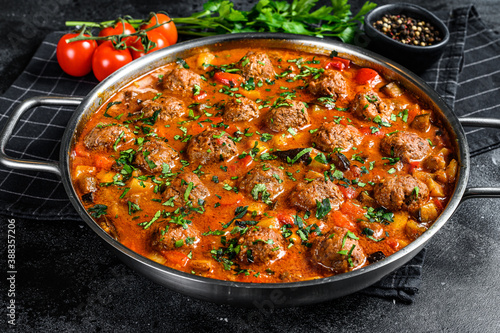 Pork meatballs with tomato sauce and vegetables in a pan. Black background. Top view