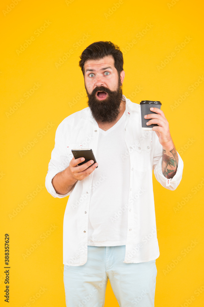 brutal hipster drinking takeaway beverage from cup. guy with beard and moustache use mobile phone for communication. morning routine. shocked bearded man hold phone while drink coffee. brutal hipster drinking takeaway beverage from cup. guy with beard and moustache use mobile phone for communication. morning routine. shocked bearded man hold phone while drink coffee.